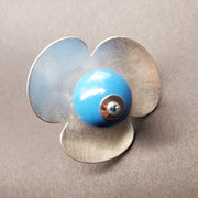 Ring with a large blue bead topped with a blue topaz rests amid 3 large rounded petals of sterling silver, 4 x 2 cm.
