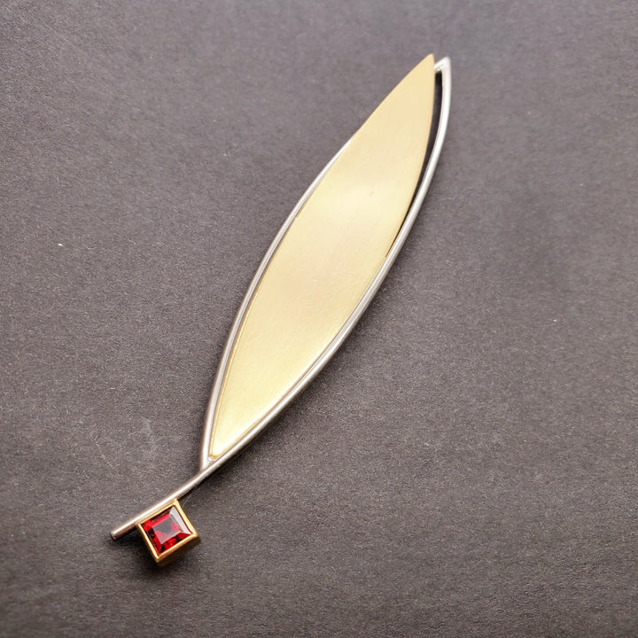A large leaf of 18k yellow gold lifts up from its white gold frame of this brooch that has a garnet detail. Brooch measures 9.5 x 2 x 1 cm.