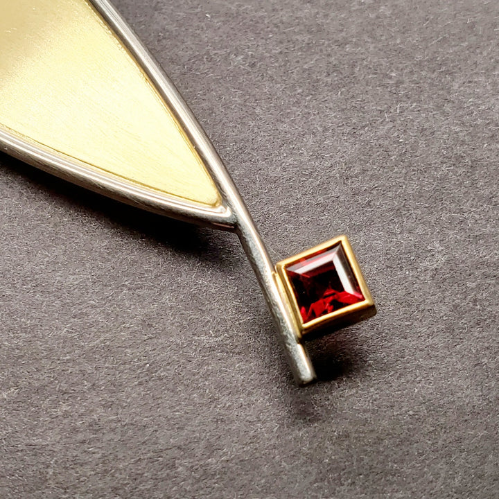 A large leaf of 18k yellow gold lifts up from its white gold frame of this brooch that has a garnet detail. Brooch measures 9.5 x 2 x 1 cm.