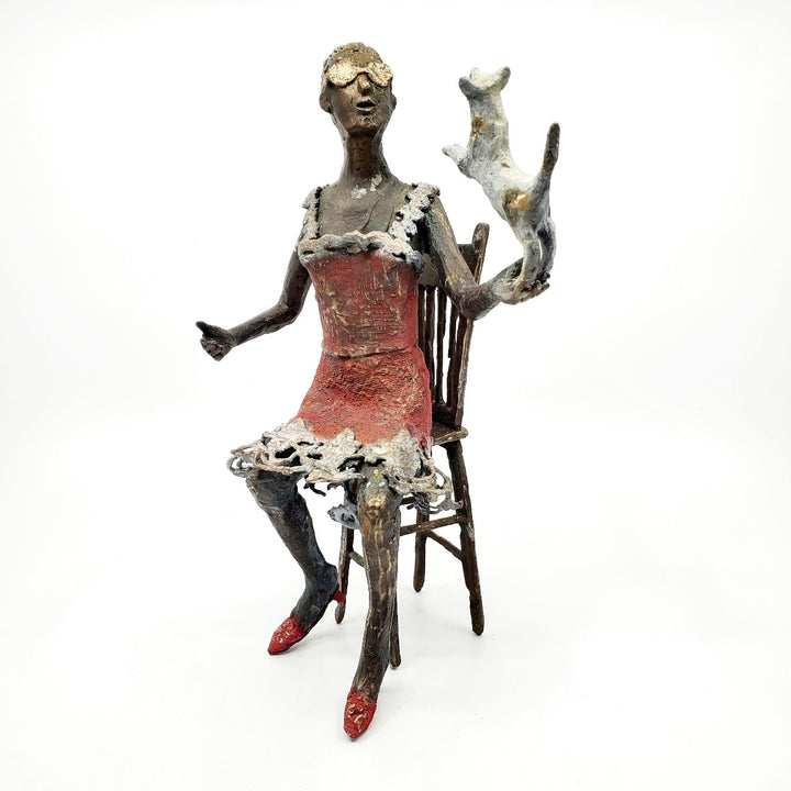 Table Talk.  A bronze figure of a woman in sunglasses sits in a tall chair, in dialogue with her small dog. Her left foot lifts away from her high heel in an active pose. Notable also are the lace details in the hem and straps of her red dress.  1 of 1.