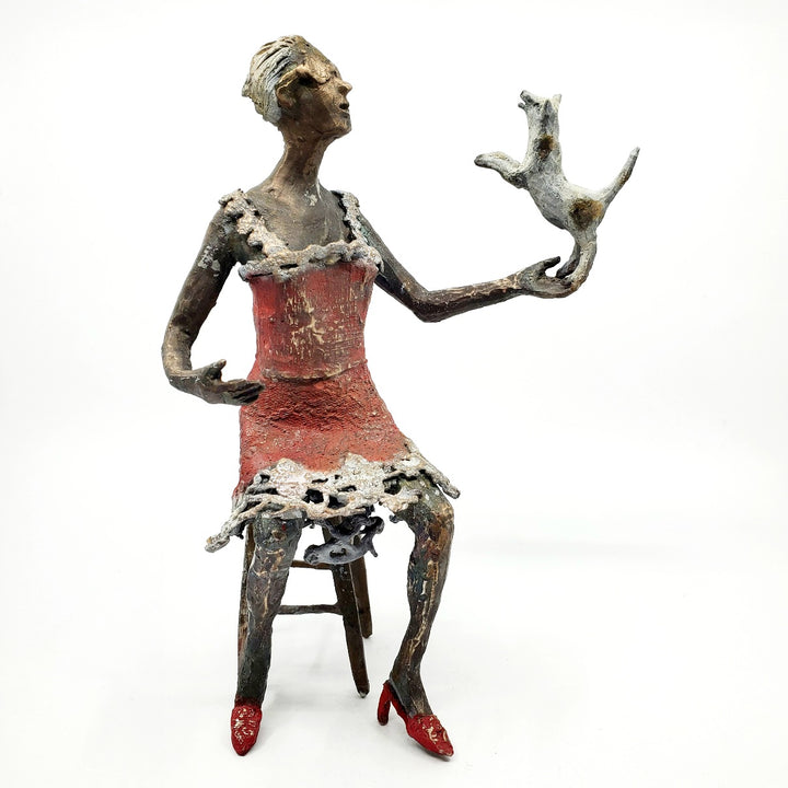 Table Talk.  A bronze figure of a woman in sunglasses sits in a tall chair, in dialogue with her small dog. Her left foot lifts away from her high heel in an active pose. Notable also are the lace details in the hem and straps of her red dress.  1 of 1.