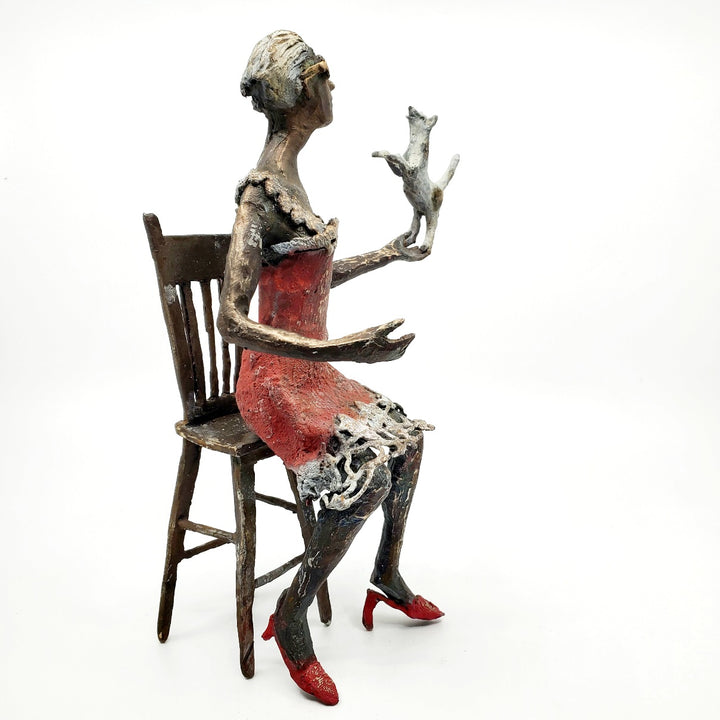 Table Talk.  A bronze figure of a woman in sunglasses sits in a tall chair, in dialogue with her small dog. Her left foot lifts away from her high heel in an active pose. Notable also are the lace details in the hem and straps of her red dress.  1 of 1.