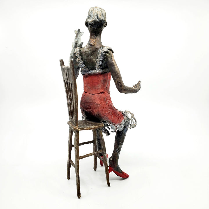 Table Talk.  A bronze figure of a woman in sunglasses sits in a tall chair, in dialogue with her small dog. Her left foot lifts away from her high heel in an active pose. Notable also are the lace details in the hem and straps of her red dress.  1 of 1.