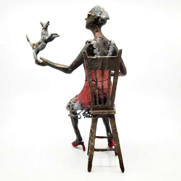 Table Talk.  A bronze figure of a woman in sunglasses sits in a tall chair, in dialogue with her small dog. Her left foot lifts away from her high heel in an active pose. Notable also are the lace details in the hem and straps of her red dress.  1 of 1.