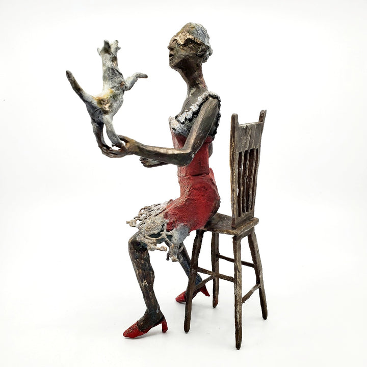 Table Talk.  A bronze figure of a woman in sunglasses sits in a tall chair, in dialogue with her small dog. Her left foot lifts away from her high heel in an active pose. Notable also are the lace details in the hem and straps of her red dress.  1 of 1.