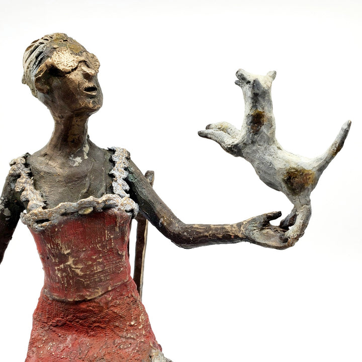 Table Talk.  A bronze figure of a woman in sunglasses sits in a tall chair, in dialogue with her small dog. Her left foot lifts away from her high heel in an active pose. Notable also are the lace details in the hem and straps of her red dress.  1 of 1.