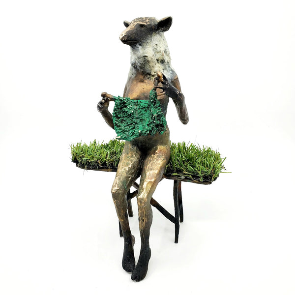 Domestic Sheep: Elsie Mae.  A bronze figure with a sheep's head and a woman's body sits on a turf-covered bench, peacefully knitting. 1 of 1.