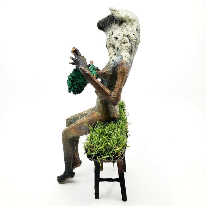 Domestic Sheep: Elsie Mae.  A bronze figure with a sheep's head and a woman's body sits on a turf-covered bench, peacefully knitting. 1 of 1.