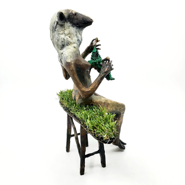 Domestic Sheep: Elsie Mae.  A bronze figure with a sheep's head and a woman's body sits on a turf-covered bench, peacefully knitting. 1 of 1.