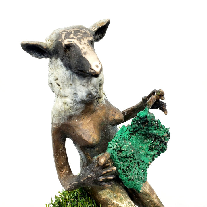 Domestic Sheep: Elsie Mae.  A bronze figure with a sheep's head and a woman's body sits on a turf-covered bench, peacefully knitting. 1 of 1.