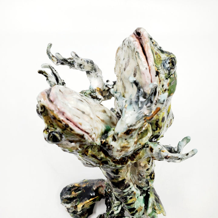 Porcelain sculpture of two frogs in an embrace, leaping together from the water. Pond growth reaches up around their feet. Richly textured with both colour and line, these spotted green frogs are streaked with gold lustre. 