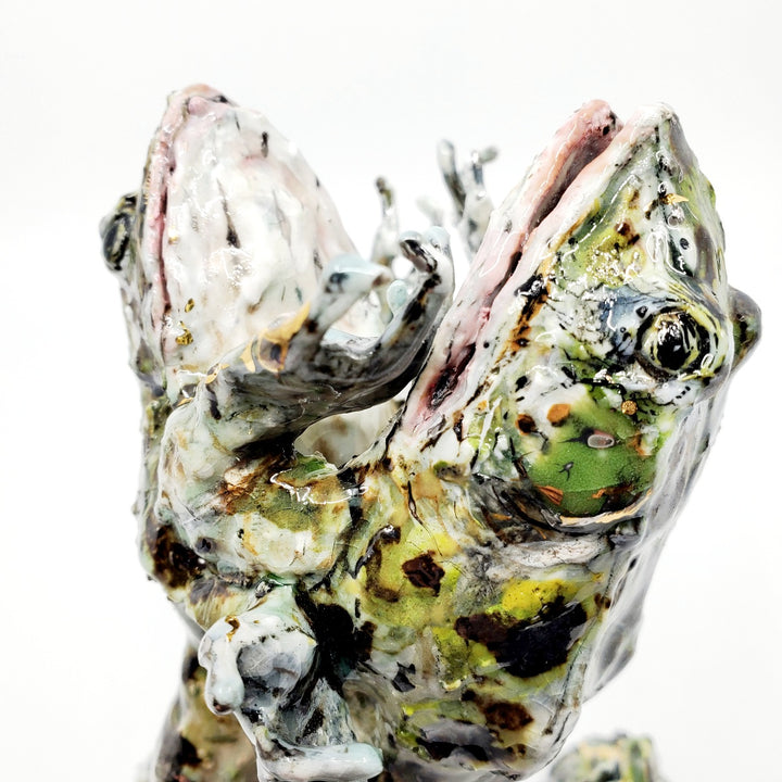 Porcelain sculpture of two frogs in an embrace, leaping together from the water. Pond growth reaches up around their feet. Richly textured with both colour and line, these spotted green frogs are streaked with gold lustre. 