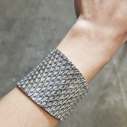 Sterling silver cuff, stamped with a geometric pattern. Within the pattern, there is a subtle texture in the oxidized spaces between the bright silver lines.