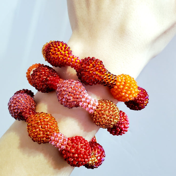 Small Red Ball Bracelet. Pink, red, and orange glass beads are woven together with orange thread. 