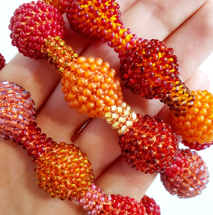 Small Red Ball Bracelet. Pink, red, and orange glass beads are woven together with orange thread. 
