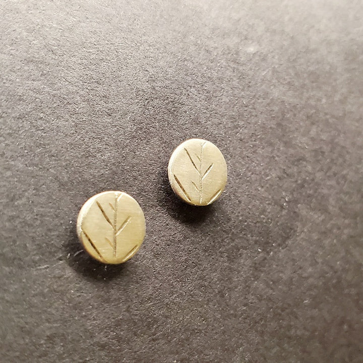 Tiny circular stud earrings in sterling silver with the delicate tracing of twigs on the surface.