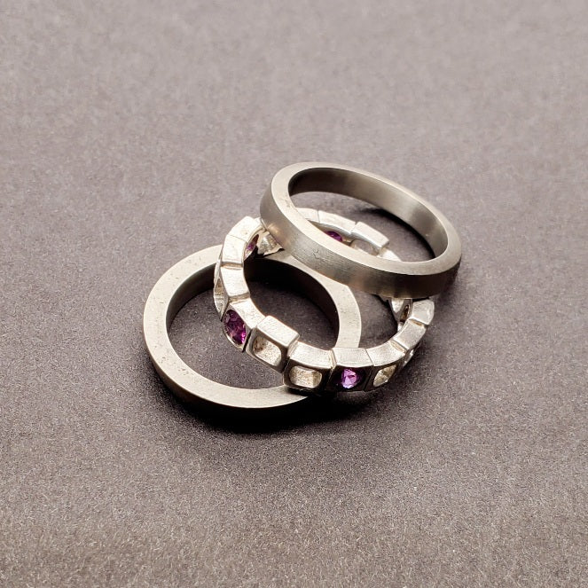 Geometrica stacking ring set with 5 purple sapphires interspaced across the staggered cubes of the sterling silver band, best worn between the 2 titanium bands.