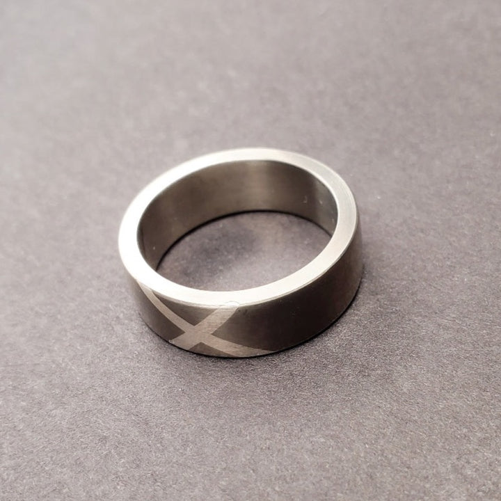A sweeping fine silver "X" marks the spot, impeccably inlaid on the 7 mm titanium band. Size 9.