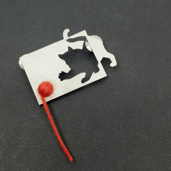 Sterling silver cut-out cat with red cotton thread. This playful pin has two locking pin backs.
