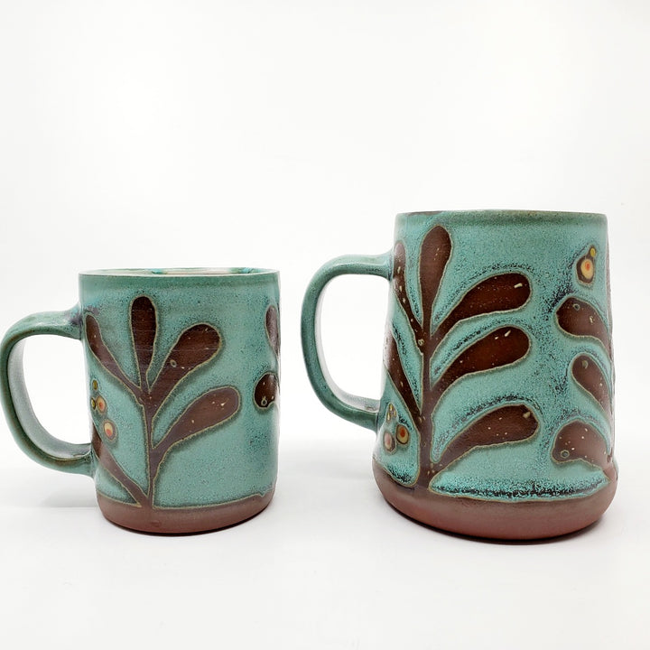 Green ceramic mug with a tactile decorated surface revealing the red clay. The interior is glazed white.  Measures approx. 8 x 10.5 x 10cm.  (Left)
