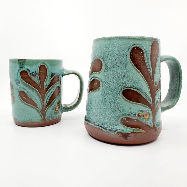 Green ceramic stein (pictured on the right) with a tactile decorated surface revealing the red clay. The interior is glazed white.  Measures approx. 8.5 x 11.5 x 12cm