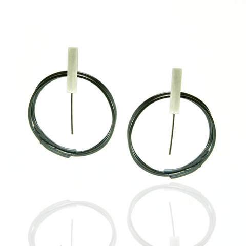Audrée H. St-Amour Triple floating hoops earrings (earhook). 3 thin oxidized hoops hanging from a bright rectangular bar. Earhook backing.