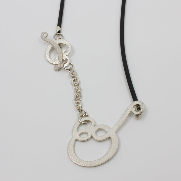 A rolling paisley pattern with a strongly stippled texture on the sterling silver motif which incidentally functions as a holder for your reading glasses. It measures 60 cm or 24" length on the black rubber chain.