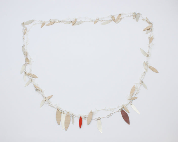 A long, loosely-knotted  white linen thread neckpiece with birch plywood leaves, one painted orange is married to a sterling silver link chain with silver leaves--and one red copper leaf. Delicately balanced together, they can be worn singly. 42"/106 cm.