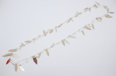 A long, loosely-knotted  white linen thread neckpiece with birch plywood leaves, one painted orange is married to a sterling silver link chain with silver leaves--and one red copper leaf. Delicately balanced together, they can be worn singly. 42"/106 cm.