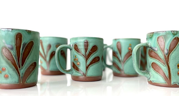Green ceramic mug with a tactile decorated surface revealing the red clay. The interior is glazed white.