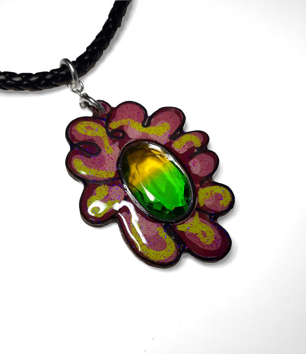 Sketchbook flower pendant. Colourful purple and green flower pendant with a sparkling yellow and green glass stone at its center. The pendant is glitter resin-coated copper, and hangs from a 16" (40cm) braided faux leather cord. 