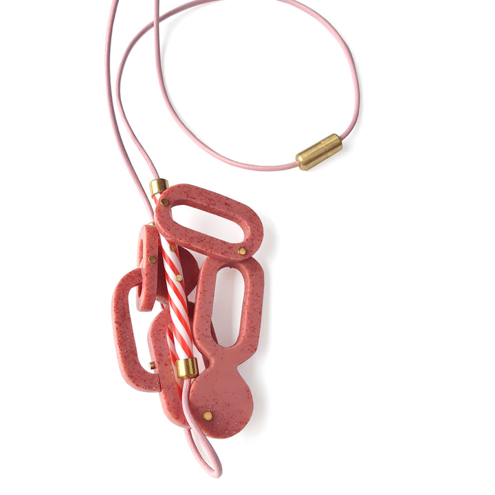 Strawberry Milkshake Necklace.  Large pink glitter resin components are riveted together with brass and capture a pair of red-striped plastic straws,  On a pink leather cord, the brooch measures 12 x 7 x 3 and hangs 42 cm in length.