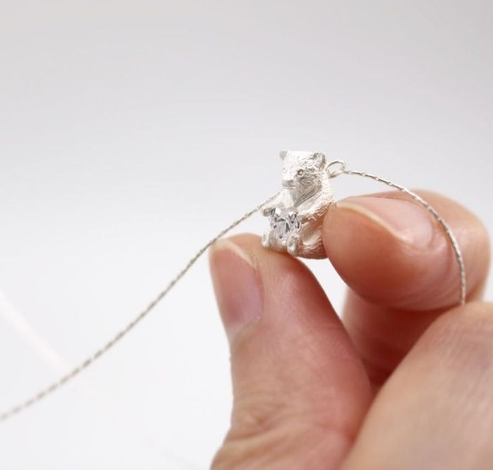 Heart Hugger. Bear pendant necklace of sterling silver, with a heart-shaped Swarovski cubic zirconia crystal. This mini bear is 1.2 cm high.