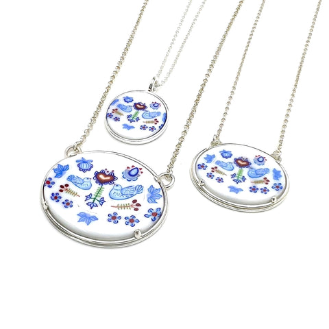 'Gingerbread heart': oval pendant in murrine glass on a 19" sterling silver chain. Birds and flowers are depicted in blue against a white background.