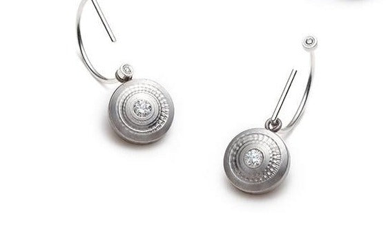 The Revolutio Collection. These earrings are made from reclaimed titanium, taken from the waste bin of a titanium aerospace supplier and lab-grown diamonds. The textures are worked on a lathe. 12mm disks, 2 x 2.3mm diamonds.
